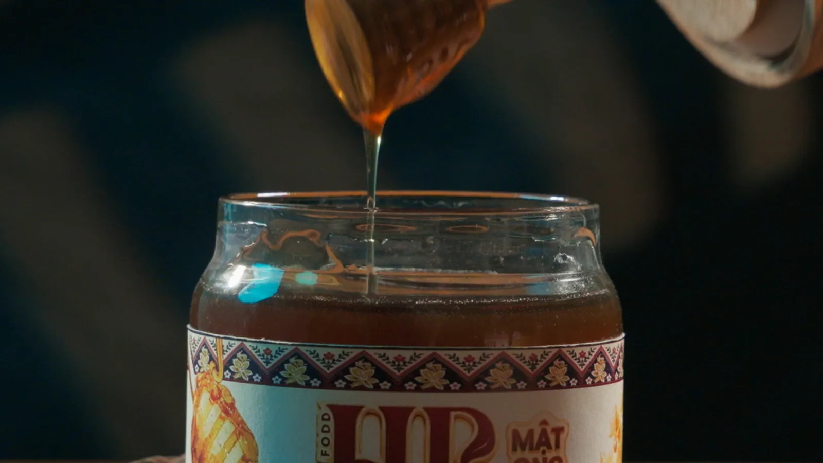 A honey dipper dripping into an open HB jar
